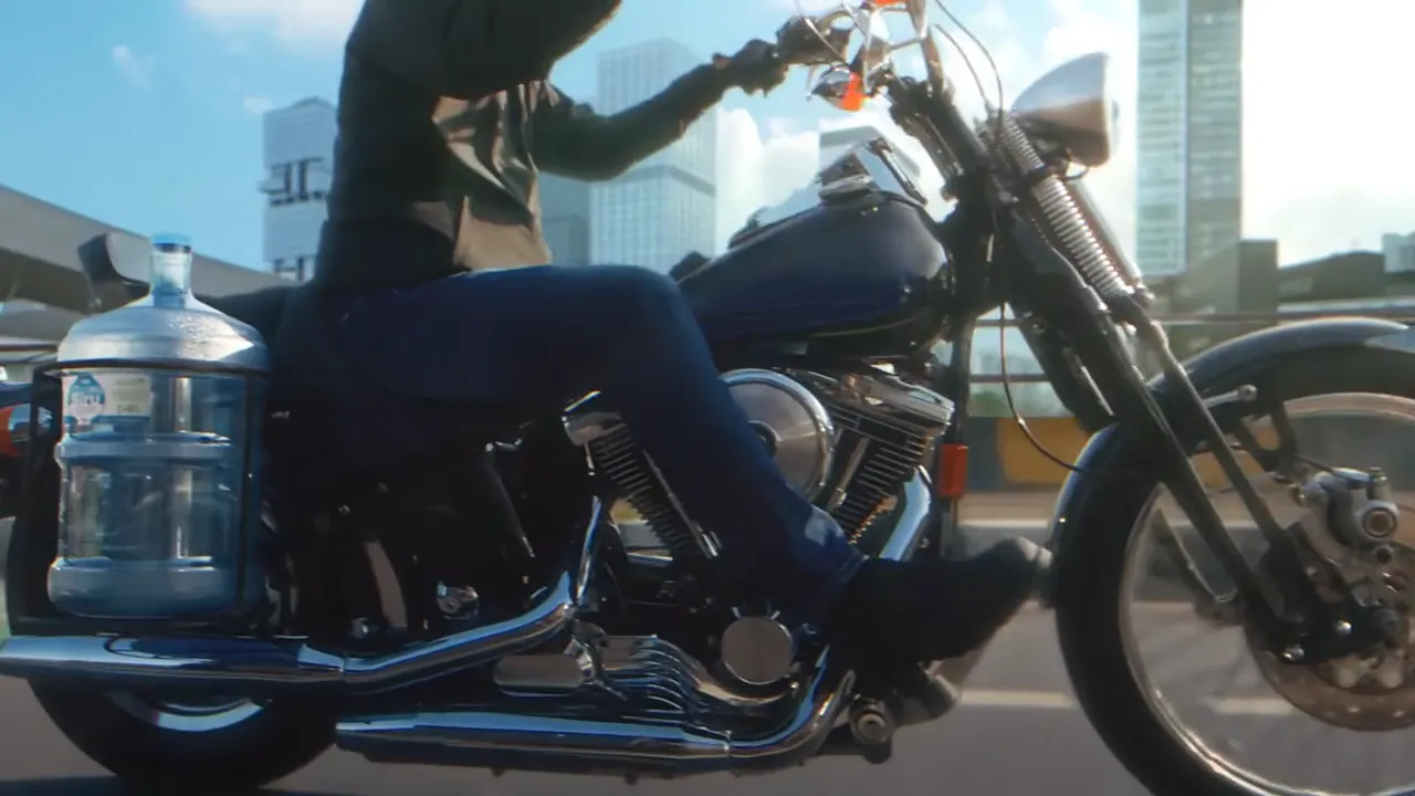 An Air Minum Biru water gallon strapped to a motorcycle on a city street